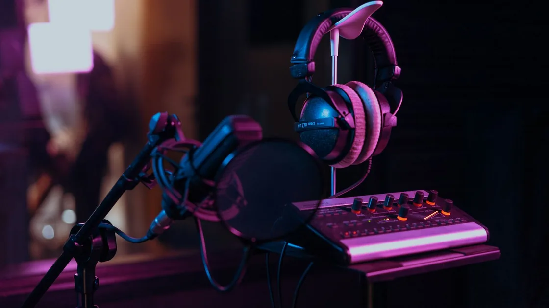 Mesa de grabación con micrófono, auriculares y superficie de control en un estudio de sonido en penumbra